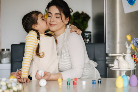 Adorable little girl kiss her mom in cheek during they painting easter eggsの写真素材