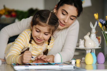 Happy laughing little girl painting picture with mom at the table in the kitchen. Easter holiday. Spring timeの写真素材