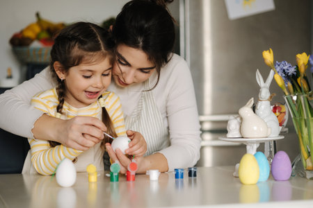 Portrait of happy smiled mom and daughter painting easter eggs on kitchen. Spring holidays mood. Familyの写真素材
