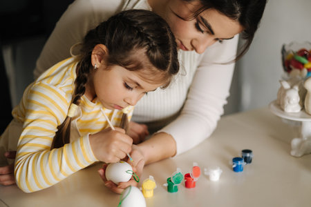 Portrait of mom and daughter painting easter eggs on kitchen. Spring holidays mood. Familyの写真素材