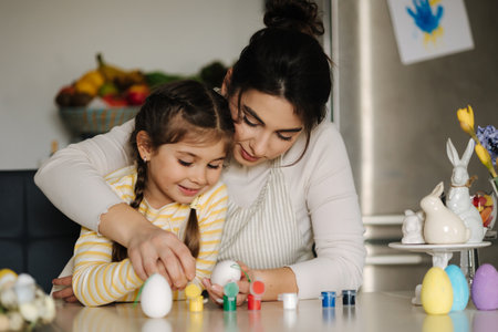 Portrait of happy smiled mom and daughter painting easter eggs on kitchen. Spring holidays mood. Familyの写真素材
