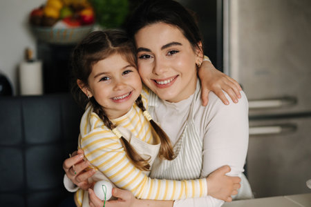 Close-up portrait of daughter with mom on kitchen. Beautiful girls dressed in apronの写真素材