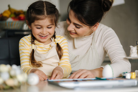 Happy laughing little girl painting picture with mom at the table in the kitchen. Easter holiday. Spring timeの写真素材