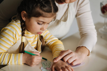 Mom and her cute little girl sitting at the table in the kitchen and color the picture with pencilsの写真素材