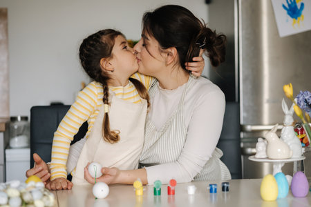 Cute little girl with her mother preparing for painting easter eggs. Mom kiss her daughterの写真素材