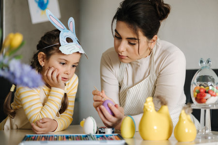 Easter time with family. Adorable girl wore bunny mask and help mom painting eggs. Spring decoration in kitchenの写真素材