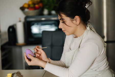 Attractive young woman painting Easter eggs in purple color using a brush. Spring holidays.の写真素材