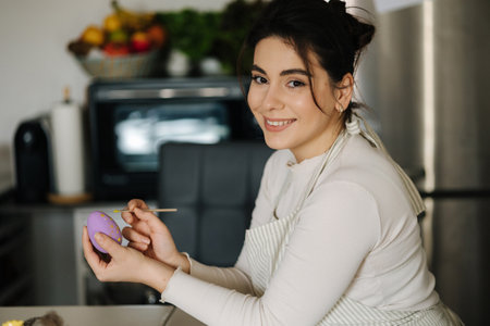 Attractive young woman painting Easter eggs in purple color using a brush. Spring holidays.の写真素材