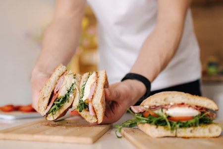 Handsome young man slice Italian sandwich and show what inside. Delicious lunch at homeの写真素材