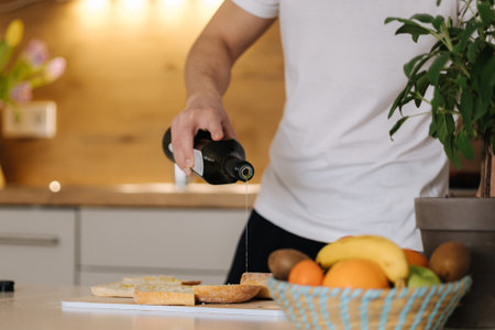Close-up of man spreads olive oil on baguette. Bright kitchen interiorの写真素材