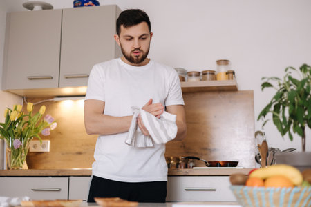 Man wipes hands with a white towel. Handsome bearded man preparing breakfast on kitchenの写真素材
