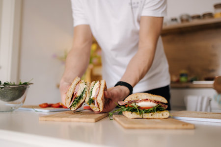 Handsome young man slice Italian sandwich and show what inside. Delicious lunch at homeの写真素材