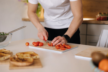 Close-up of man slice little organic tomatoes on wooden board. Red cherry tomatoの写真素材