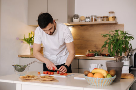 Handsome man take and slice little organic tomatoes on wooden board. Red cherry tomatoの写真素材
