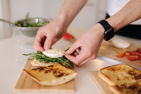 Human hand put piece of mozzarella on sandwich with arugula. Classic Italian foodの写真素材