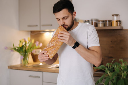 Handsome bearded man smell a freshly baked baguette. Home food conceptの写真素材