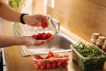 Close-up of human hand take red cherry tomatoes in the kitchenの写真素材