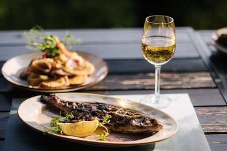 Baked seabass fish in the oven served with slice of lemon baked potatoes and glass of vine.の写真素材