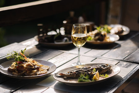 Dinner on summer terrace. Several dishes of fish and some meat in restaurant. Glasses with vine