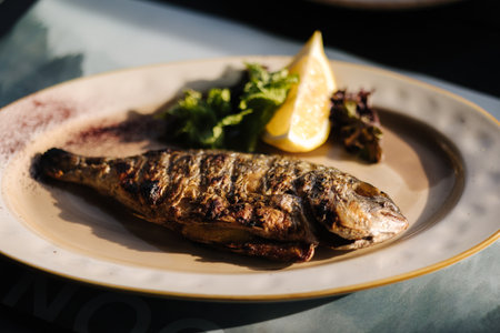 Roasted dorado fish with slice of lemon served on beautiful plateの写真素材