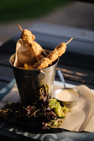 French fries and meat on wooden sticks served in a metal bucket with sauce and greensの写真素材