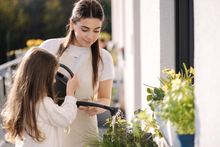 Mom watering plant with her adorable little daughter. Happy family gardening on balconyの写真素材