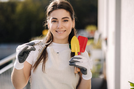 Portrait of beautiful woman in overall with garden tools stand at balcony and preparing for landing....