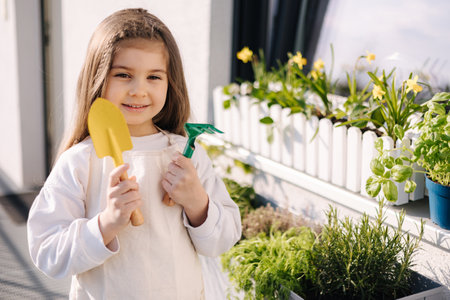 Portrait of adorable little girl hold a small shovel and a rake and prepare for landing on balconyの写真素材