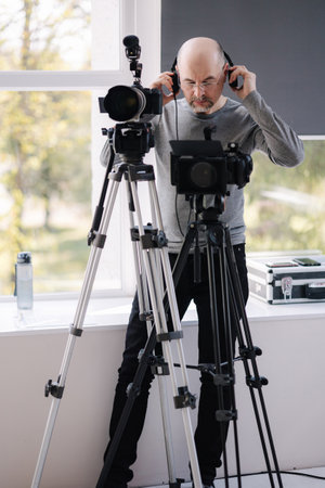 An experienced cameraman shoots a video in the studio. Man uses camera and tripods. Professional audio equpmentの写真素材