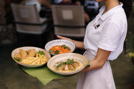 Side view of female waitress told tree dishes on tray. Middle selection of woman bring food to clientsの写真素材
