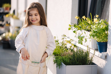 Beautiful girl try fresh ripe crop of greens from own flowerbed on balcony. Smiled little girlの写真素材