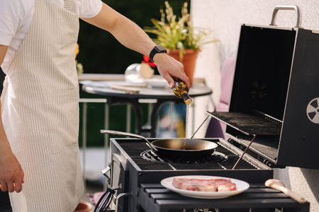Man preparing food outdoor on BBQ grill. Adding olive oil on frying pan to make T-bone Steakの写真素材