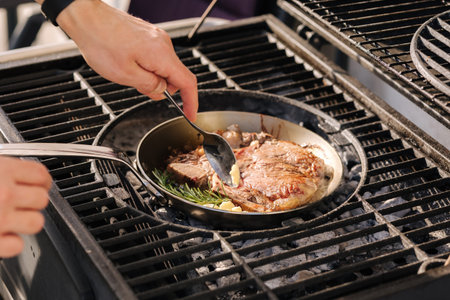 Male chef preparing T-bone steak on carbon steel frying pan outdoor on grill. BBQ concept. Close-up