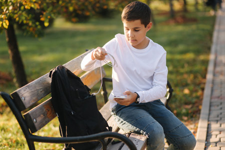 Handsome teenage boy take from his backpack powerbark for charging smarphone. Cute boy in the park in autumn timeの写真素材