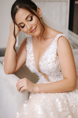 Attractive young bride sitting on chair in front of big window in her luxury house. Bride morning concept. Wedding day.の写真素材