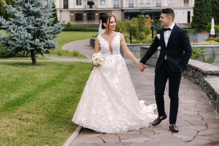 Happy newlyweds hold hands and walk around the reserve. Gorgeous wedding couple of groom and bride smileの写真素材