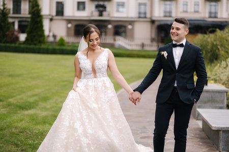 Happy newlyweds hold hands and walk around the reserve. Gorgeous wedding couple of groom and bride smileの写真素材