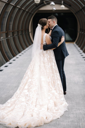 Back view of groom and bride walk in the big hall with windows. Elegant room kiss brideの写真素材