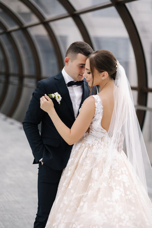 Beautiful wedding couple in the big hall with windows. Elegant bride and groom hug each otherの写真素材