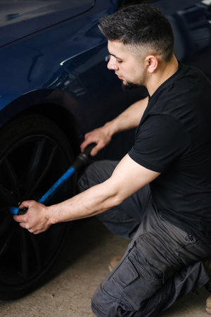 Handsome man mechanic checking tire service via insurance system at garage. Safety vehicle. Wheel checkの写真素材