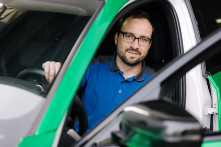 Photo of mechanic look into camera through an open car door. Man in glasses testing electronic. Car...