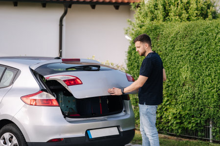 Side view of handsome man open hatchback car for trunk. Vehicle and automotive travel road trip.の写真素材