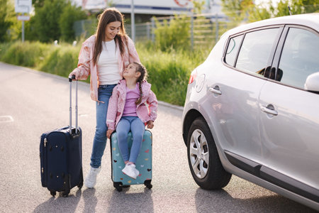 Family standing by the car with suitcases and waiting journey. Little girl sitting on kid suitcase.の写真素材