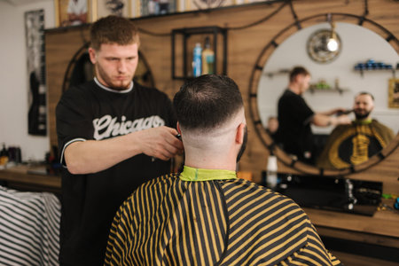 Confident bearded man visiting hairstylist in barber shop. Professional berber working