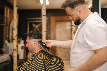 Professional hairdresser cuts hair of confident man in barbershopの写真素材