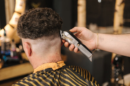 Back view of hairdresser cuts hair using trimmer. Close-up of process in barber shopの写真素材
