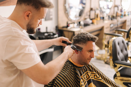Professional hairdresser cuts hair of confident man in barbershopの写真素材