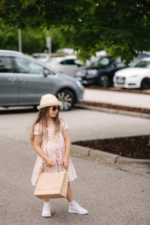 Cute little girl on shopping. Portrait of adorable kid with shopping bags and bring it to parking placeの写真素材