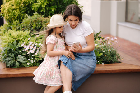 Mom and daughter looking pictures on phone. Beautiful girls using phone outdoorの写真素材