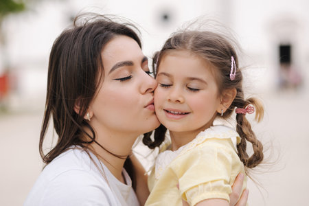 Close-up portrait of adorable daughter with beautiful mom. Woman kiss her daughterの写真素材